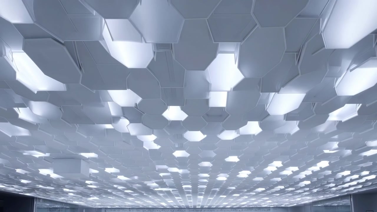Una vista verso l'alto si muove sotto piastrelle esagonali del soffitto a strati, mentre sezioni luminose illuminate si spostano attraverso l'inquadratura, enfatizzando forme ripetute, toni di grigio freddi e una forte prospettiva