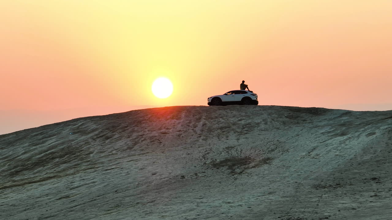 남자는 마즈다 차 위에 일출이 내려다보이는 사막 언덕에 앉아 있다