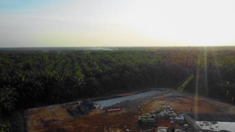 Cinematic-4K-Drone-Footage-of-Onshore-Drilling-Rig-equipment-structure-for-oil-exploration-and-exploitation-in-the-middle-of-jungle-surrounded-by-palm-oil-trees-during-sunset-and-high-oil-price