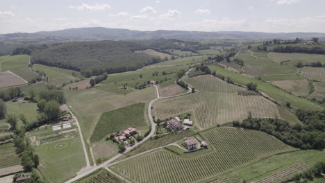 Toma-De-Drones-De-Caminos-Sinuosos-Y-Campos-Agrícolas-Dorados-En-El-Paisaje-De-Toscana-Italia-En-Un-Día-Soleado-Con-Cielo-Azul-Y-Nubes-En-El-Horizonte.