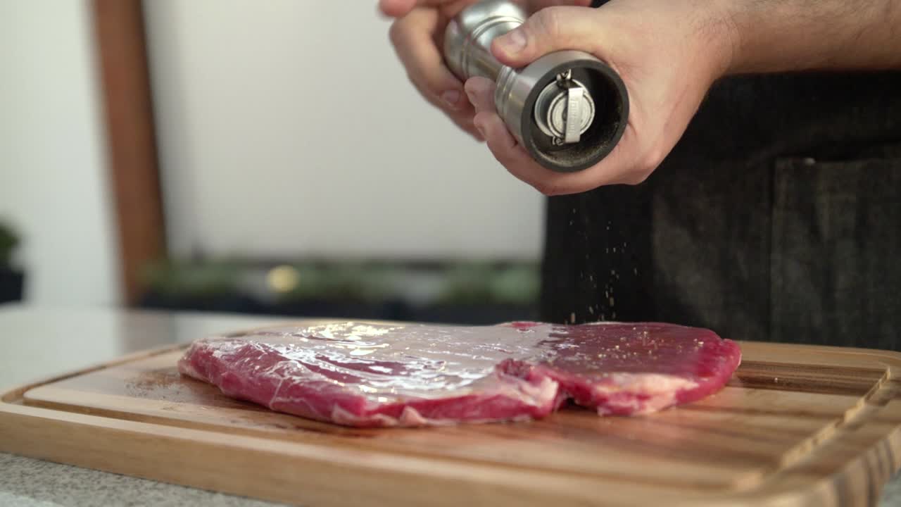 Primo piano di uno chef che aggiunge pepe a una bistecca di manzo cruda, al rallentatore