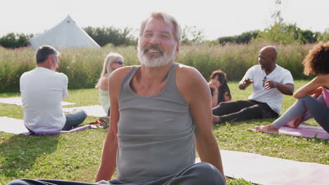 portrait of mature man on outdoor yoga retreat with friends and campsite in background