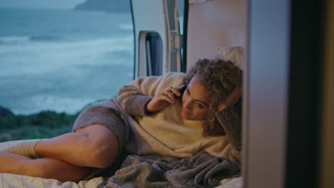 woman tourist talking cellphone lying motorhome at evening ocean coast close up.