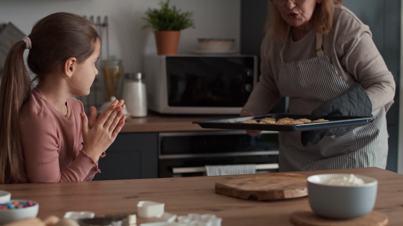 abuela y nieta sacando galletas del horno.