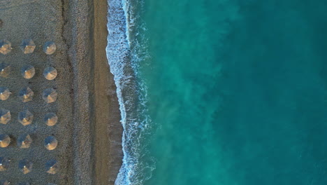 Aerial-drone-top-down-shot-over-the-beach-umbrellas-along-the-shore-of-Corinth,-Kiato,-Greece-at-daytime