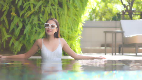joven y elegante mujer asiática pequeña parada en el agua de la piscina en un día caluroso