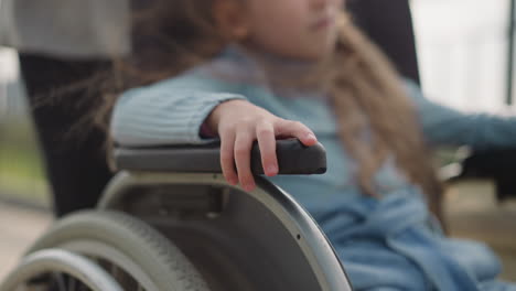 una niña pequeña se sienta en silla de ruedas con el pelo claro ondeando en el viento