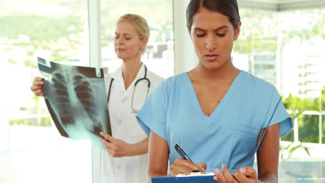 Doctor-writing-on-clipboard-with-her-colleagues-behind-