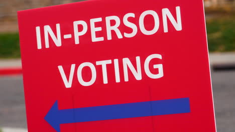 red in-person voting sign with blue arrow pointing left and blowing in the wind outside