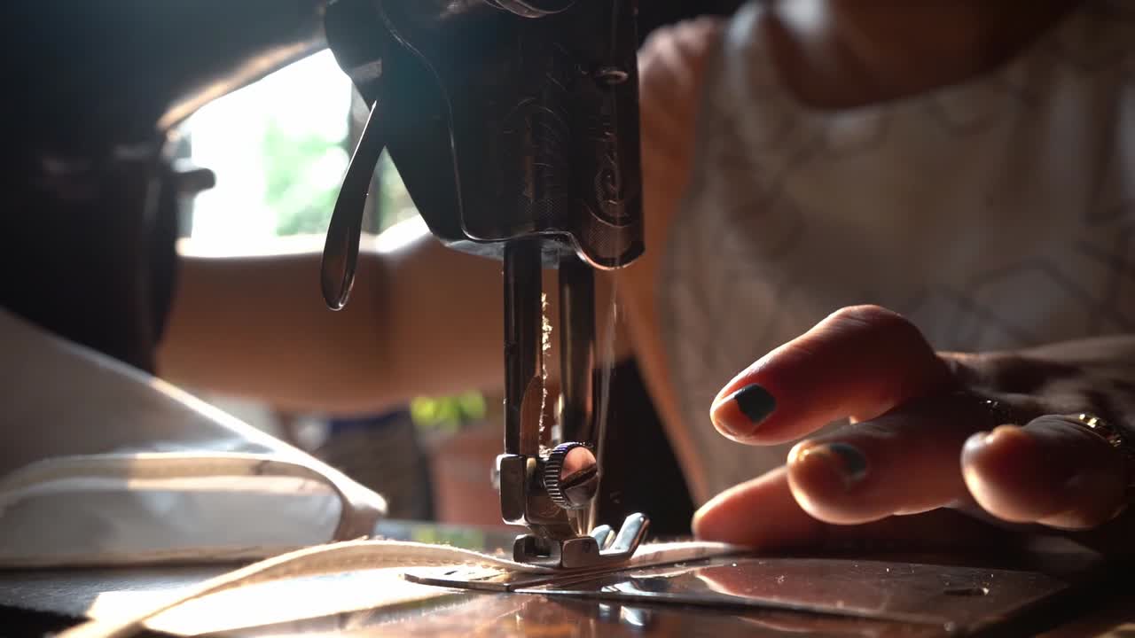 Mano di donna che cuce una striscia di tessuto di cotone bianco per realizzare una mascherina usando una macchina da cucire manuale in un negozio ad Agra, Uttar Pradesh, India - Primo piano (movimento lento).
