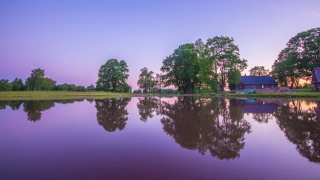 Día-Relajante-Hasta-El-Lapso-De-Tiempo-Del-Amanecer-En-Un-Lago-Reflectante-Con-Una-Pequeña-Casa-Y-árboles