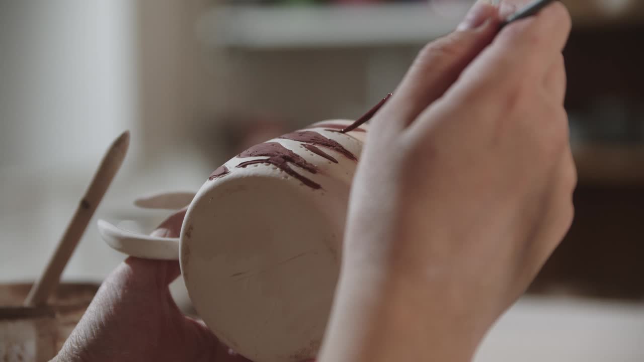 mujer joven pintando en la copa de cerámica con un pincel y color rojo