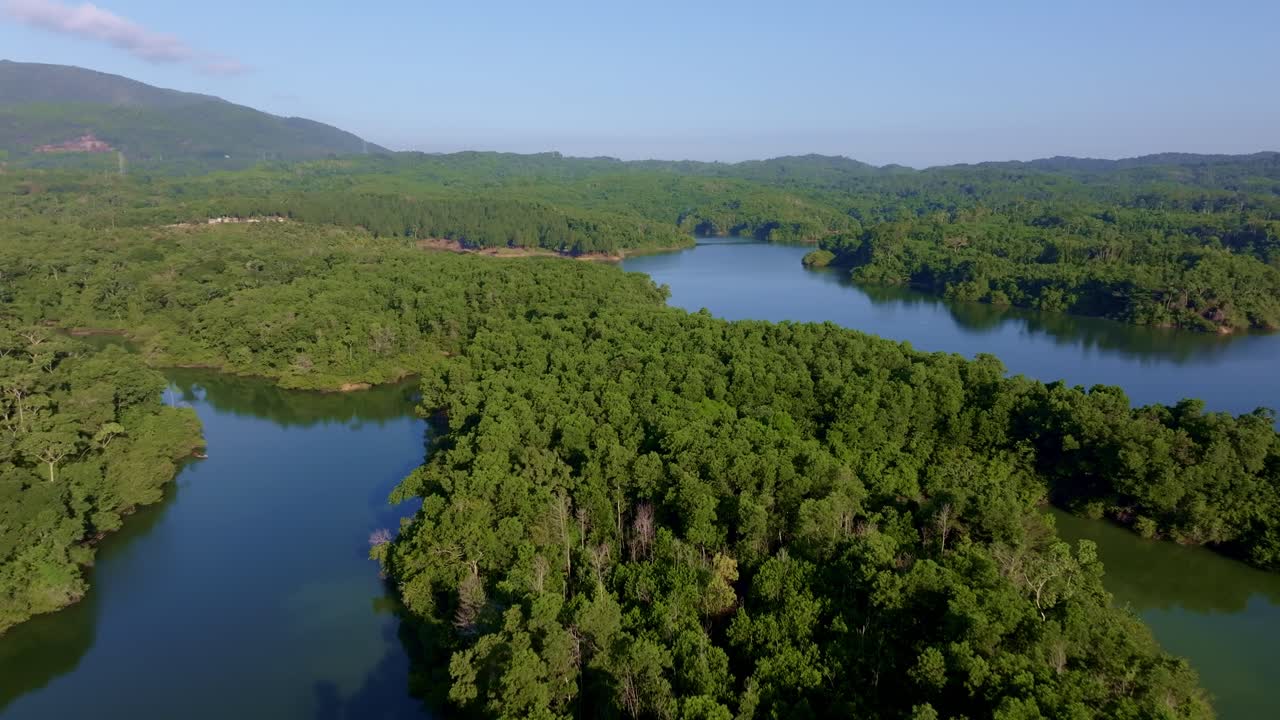 Lush green forest surrounding calm waters of Rincon Dam reservoir, Dominican Republic. Aerial forward