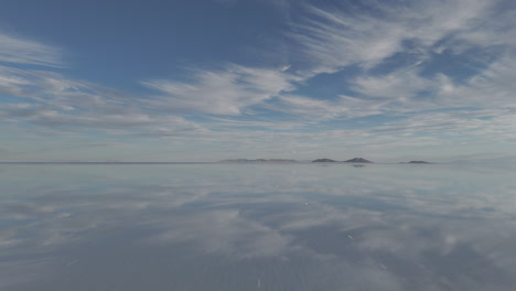 drone shot flying above the mirror salt flats in bolivia uyuni on a cloudy day with the visible reflection log