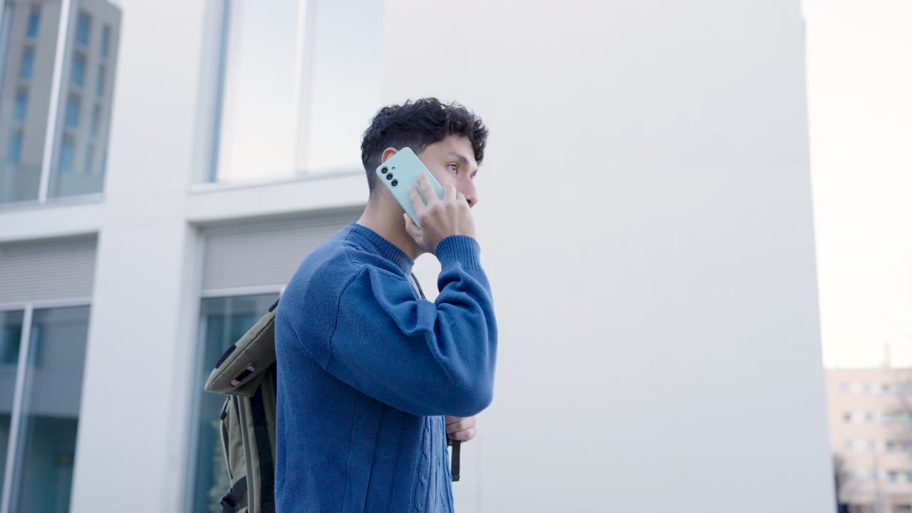 Young man with backpack walking and speaking on smartphone