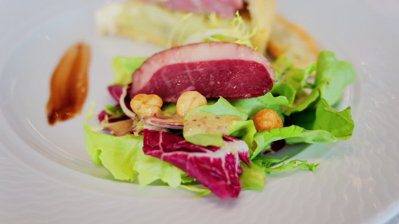 Close up of a slice of quiche featuring with a side salad and a slice of cured meat on a white plate at a restaurant