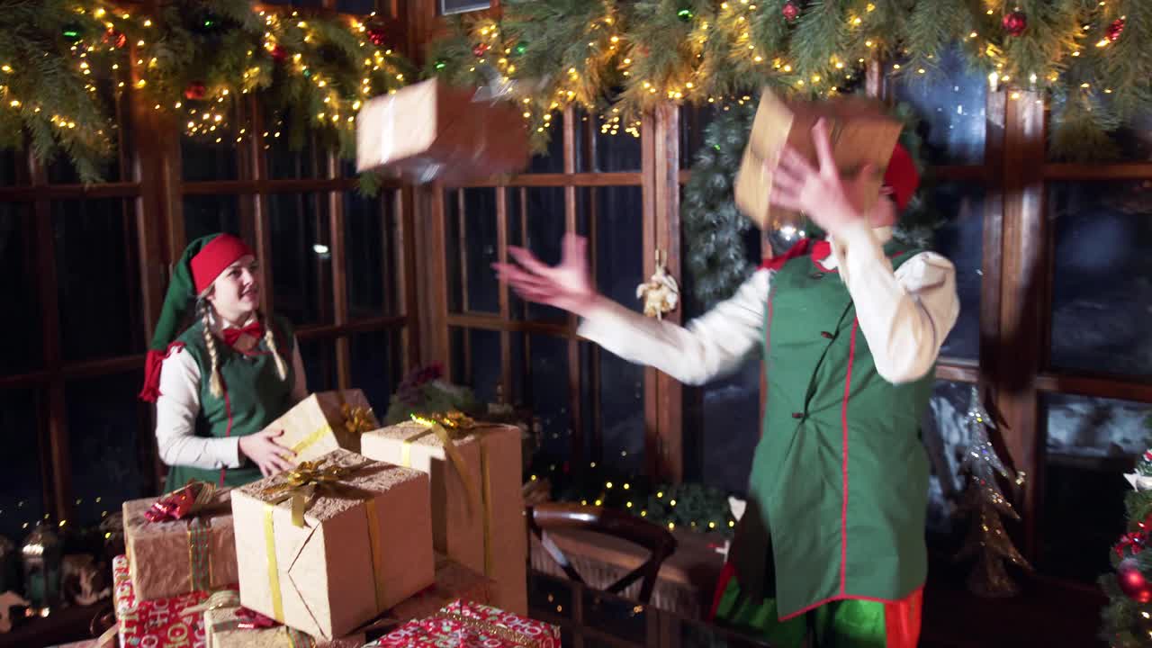 Funny elves playing with gift boxes. Naughty elf juggling with Christmas presents in Santa's residence. Festive background at winter holidays