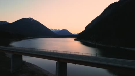 sunset aerial drone flight above the scenic and idyllic sylvensteinspeicher fresh drinking water sylvenstein reservoir bridge with mountains in the bavarian austrian alps and clear blue water below