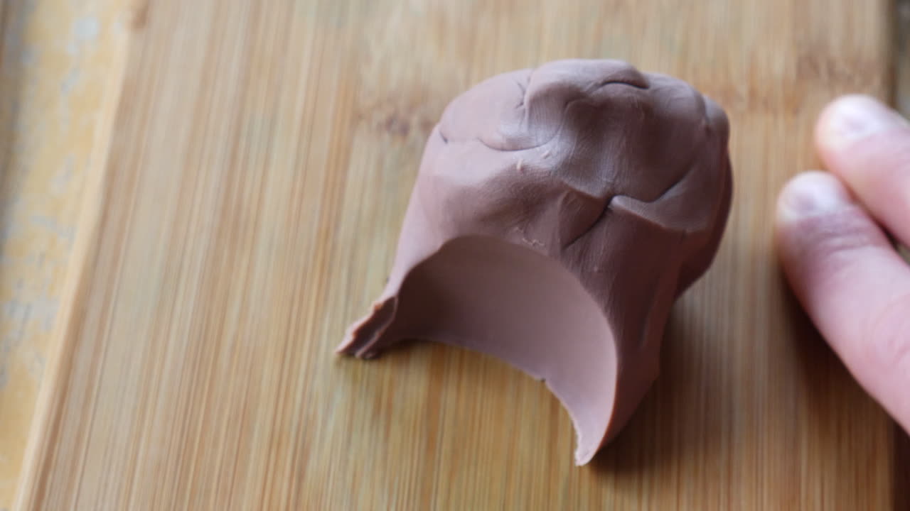 미술 스튜디오의 나무 책상에 도구로 부드러운 갈색 모델링 점토 조각을 자르고 조각하는 예술가나 조각가의 손에 가까이