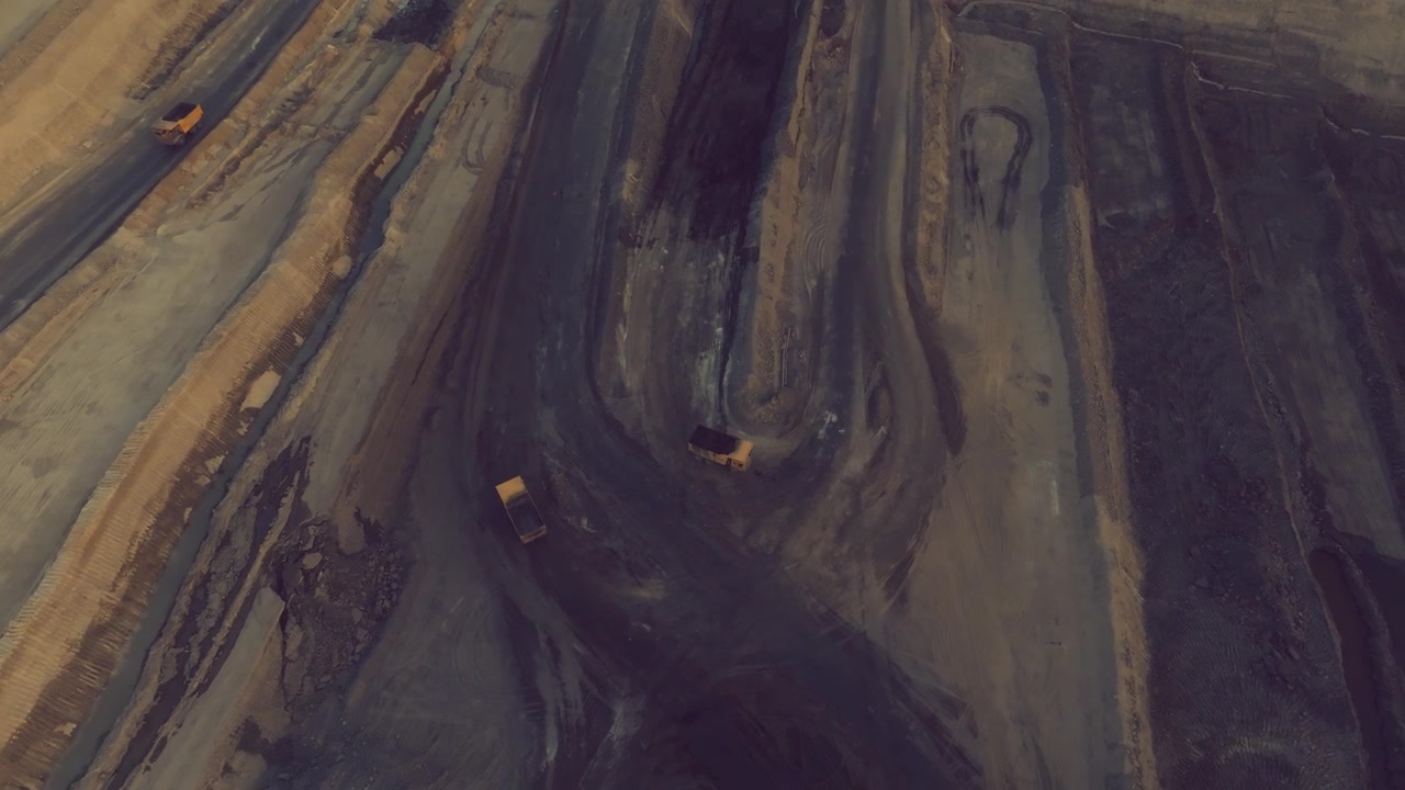 Large mining trucks follow winding tracks across layered earth at Thar Engro Coal Mining site.