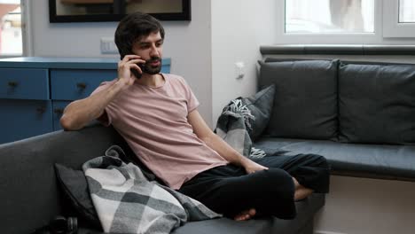 smiling bearded man calling a person, listening and talking with smartphone in home living room