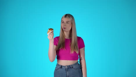 una joven rubia comiendo pasteles contra un fondo azul, toma de estudio