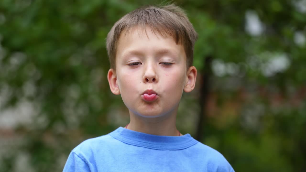 Portrait of young boy eating with mouth full outdoors. Child enjoys eating tasty donut and looking at camera in summer.