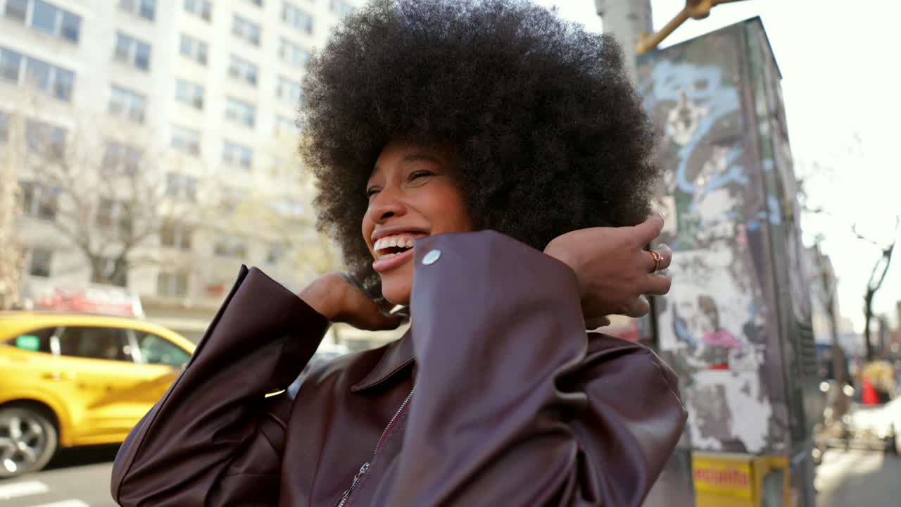 Una donna con un afro cammina lungo una strada cittadina