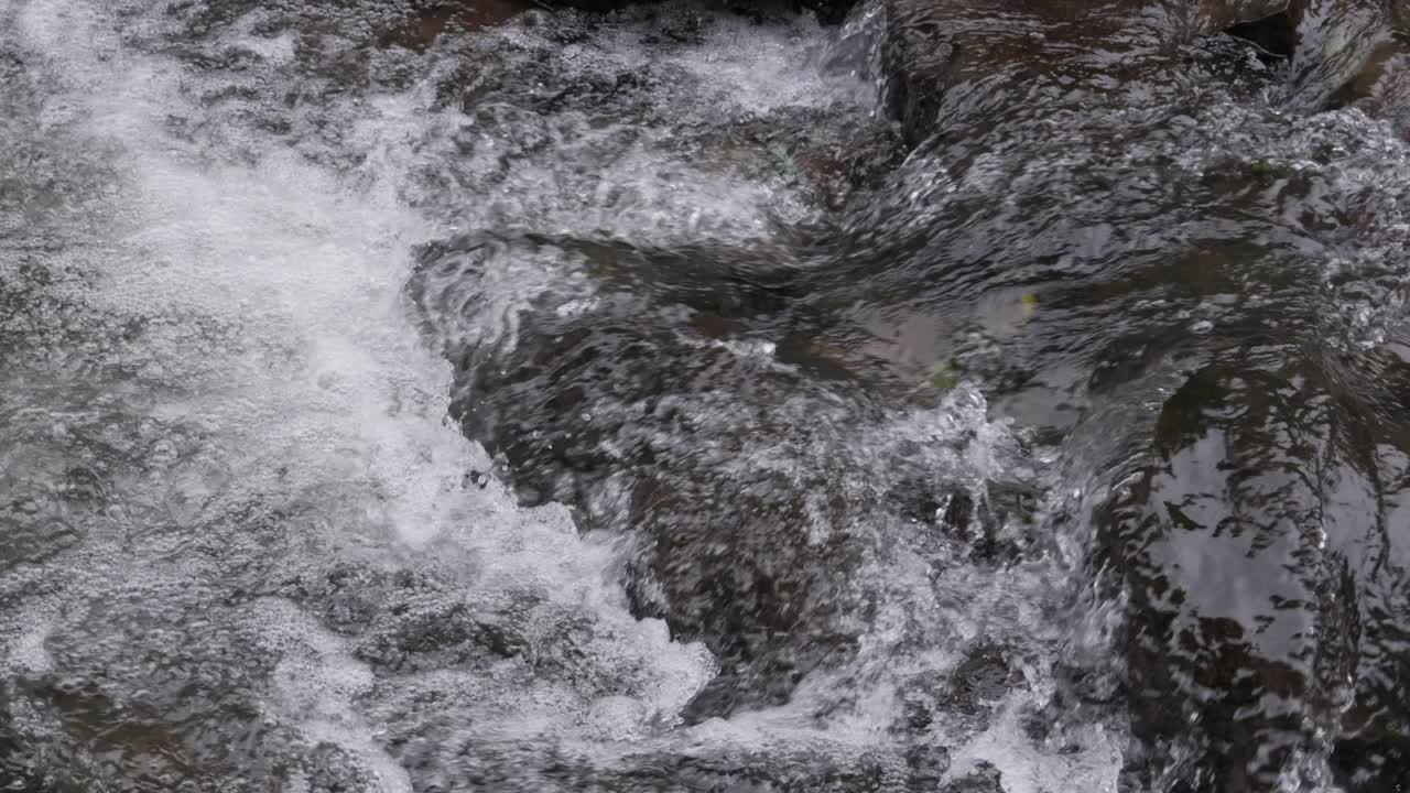 Rapid river water flowing over rocks in slow motion, creating bubbles and splashes