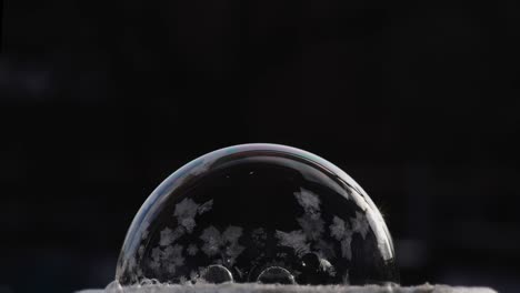 fondo de invierno festivo con patrón de hielo de globo de aire. una burbuja de jabón se encuentra en la nieve en un fondo negro, los copos de nieve caen sobre él y se congelan