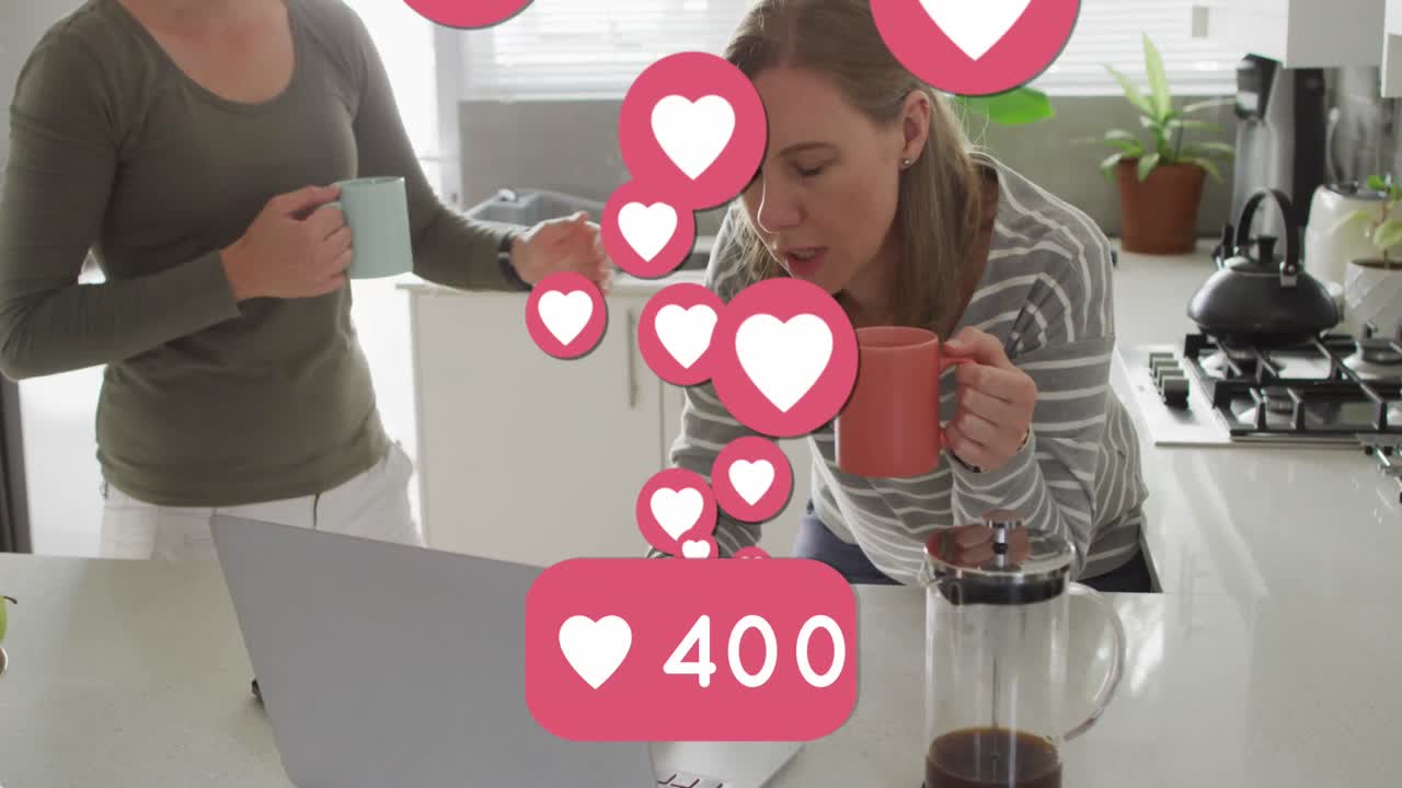 animación de emojis de corazón y números sobre una feliz pareja de mujeres caucásicas enamoradas en la cocina
