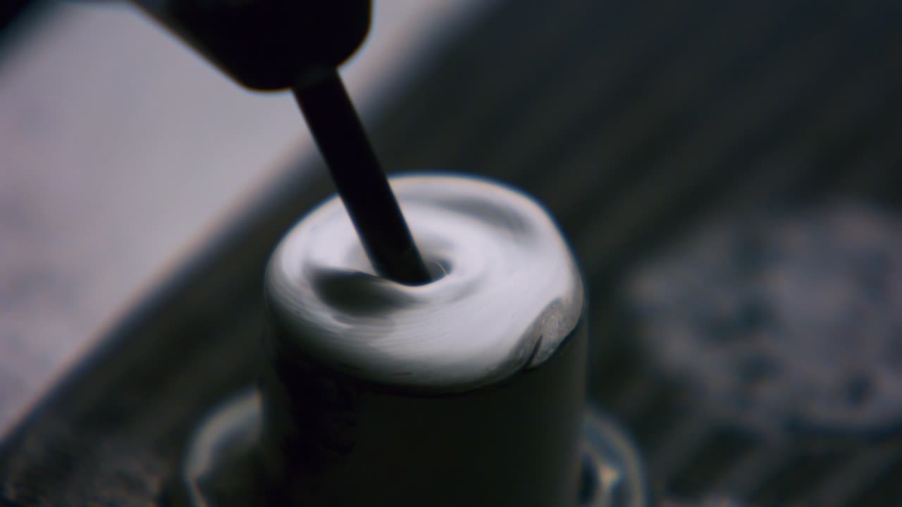 Clouseup of tattoo artist mixing ink in caps fixed with vaseline on table. Tattooist preparation, flow of dark fluid dye in container. Master tattooer loads flask with ebony paint liquid.
