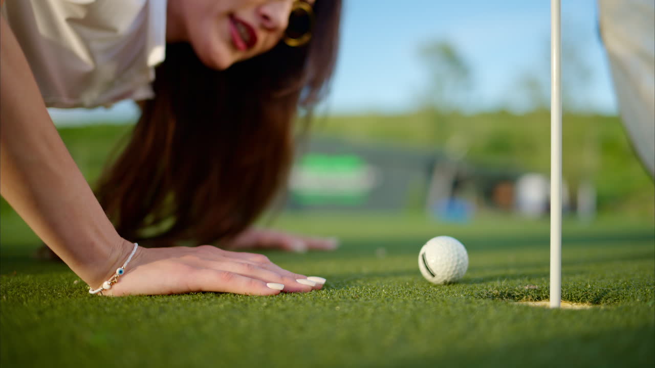 Woman trying to push a golf ball into the hole by blowing on it