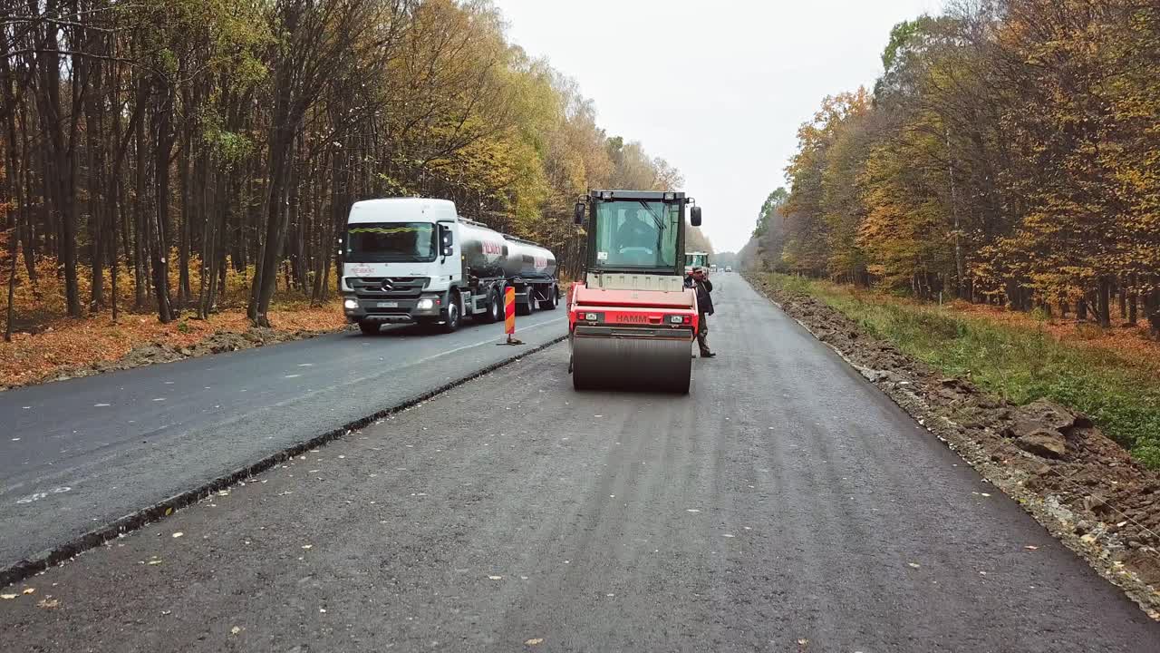 Heavy equipment while building an asphalt road. Steamroller pressing new asphalt in highway in autumn. Road works on natural background.