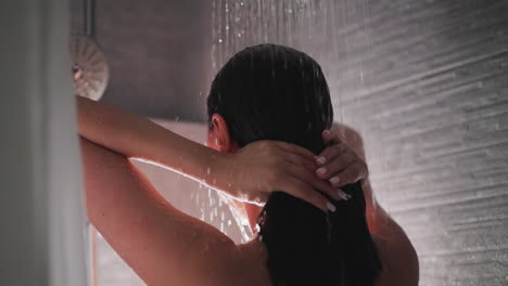 young lady using modern shower to wash hair. young lady enjoying refreshing shower in bathroom using water to wash brunette hair. bathroom routine