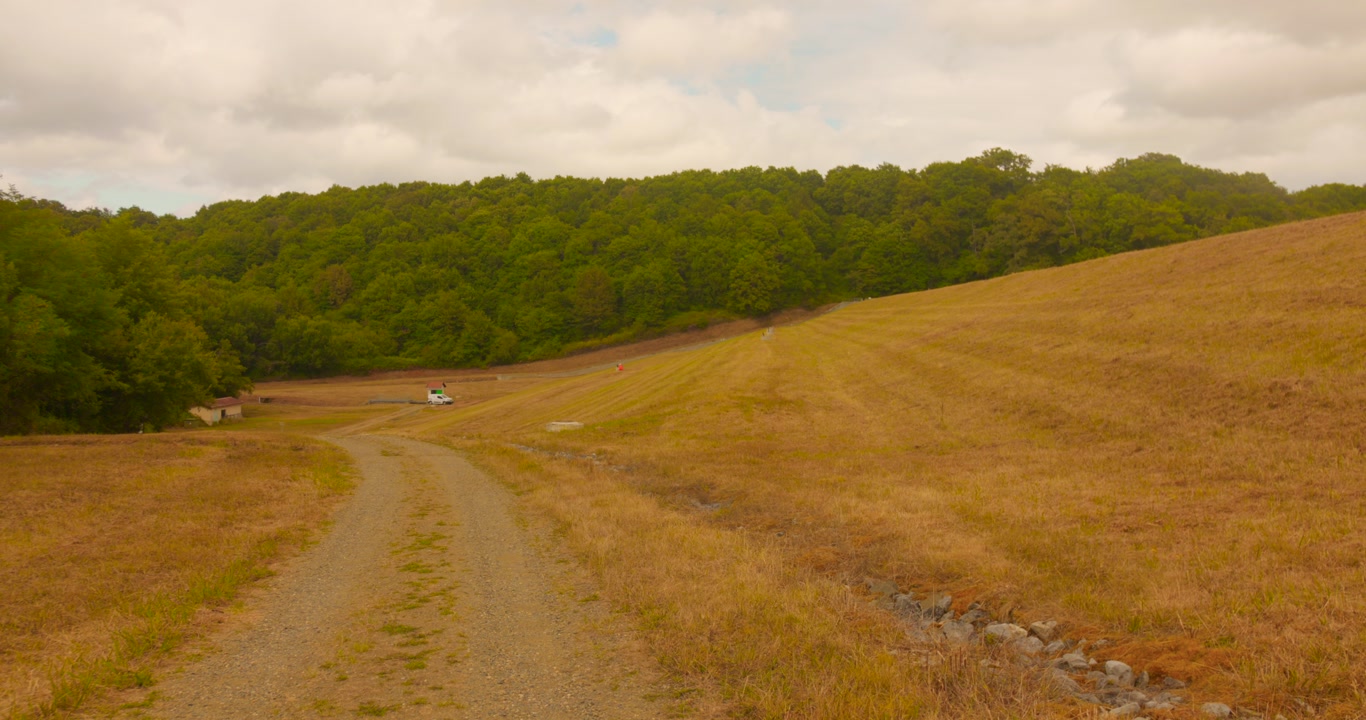 Profile view of lush greenery at distance with muddy path in foreground near Renung Dam in France.