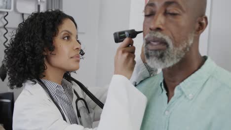 diverse female doctor examining male patient in consulting room, using otoscopy, slow motion