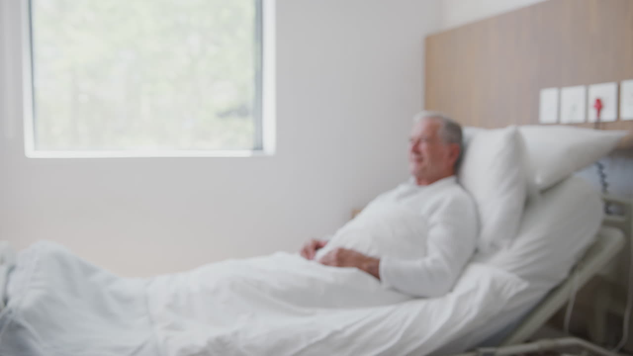 외과 의사가 노인 병원 병실에서 노인 남성 환자를 방문하고 손을 흔들고 있습니다.