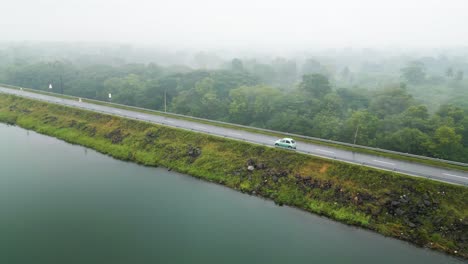 Toma-De-Seguimiento-De-Un-Vehículo-Pequeño-Que-Conduce-Cerca-Del-Embalse-De-Loggal-Oya-En-Un-Día-Lluvioso-Y-Brumoso,-Sri-Lanka