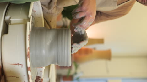 vertical male potter wearing apron sitting at workshop turntable shaping clay material