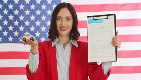 woman holding car insurance form and toy car in front of american flag