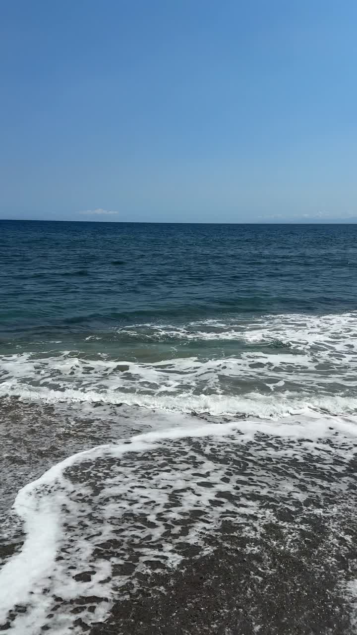Le onde dell'oceano si schiantano su una spiaggia sabbiosa sotto un cielo blu limpido
