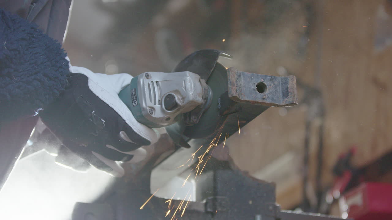 disparo de ángulo bajo hacia arriba de una mujer usando una molienda para cortar acero con chispas volando