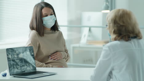 pregnant woman in mask visiting doctor in maternity clinic