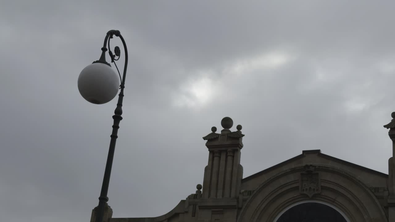 Farola con esfera de vidrio blanco frente al Mercado de Ourense en un día nublado.