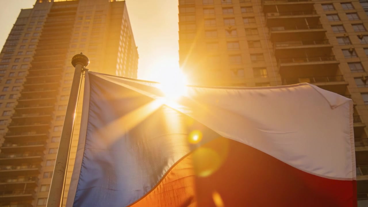 Bandiera nazionale che sventola sull'asta per la brezza, catturando il sole dorato tra le torri e creando un effetto lens flare.