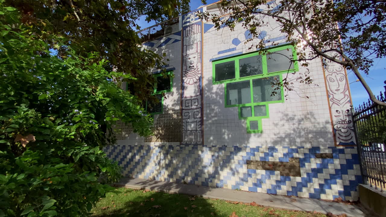 Un padiglione a tema Guatemala a Siviglia, ricoperto di piastrelle blu e bianche con uccelli tropicali e motivi culturali, circondato da alberi secolari