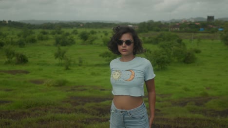 A-middle-shot-of-a-young-Indian-woman-with-sunglasses-gazes-confidently-at-the-camera-amidst-a-lush-forest-setting