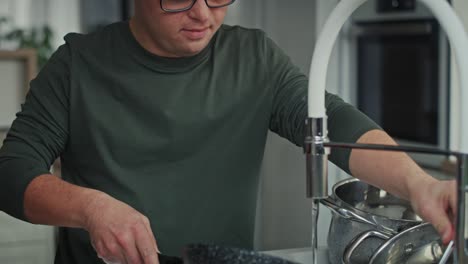 다운 증후군을  ⁇ 고 있는 성인 백인 남자가 집에서 접시를  ⁇ 고 있습니다.
