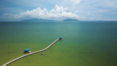 simple calm walking pier to huts jetting out into the blue green ocean with island on the horizon